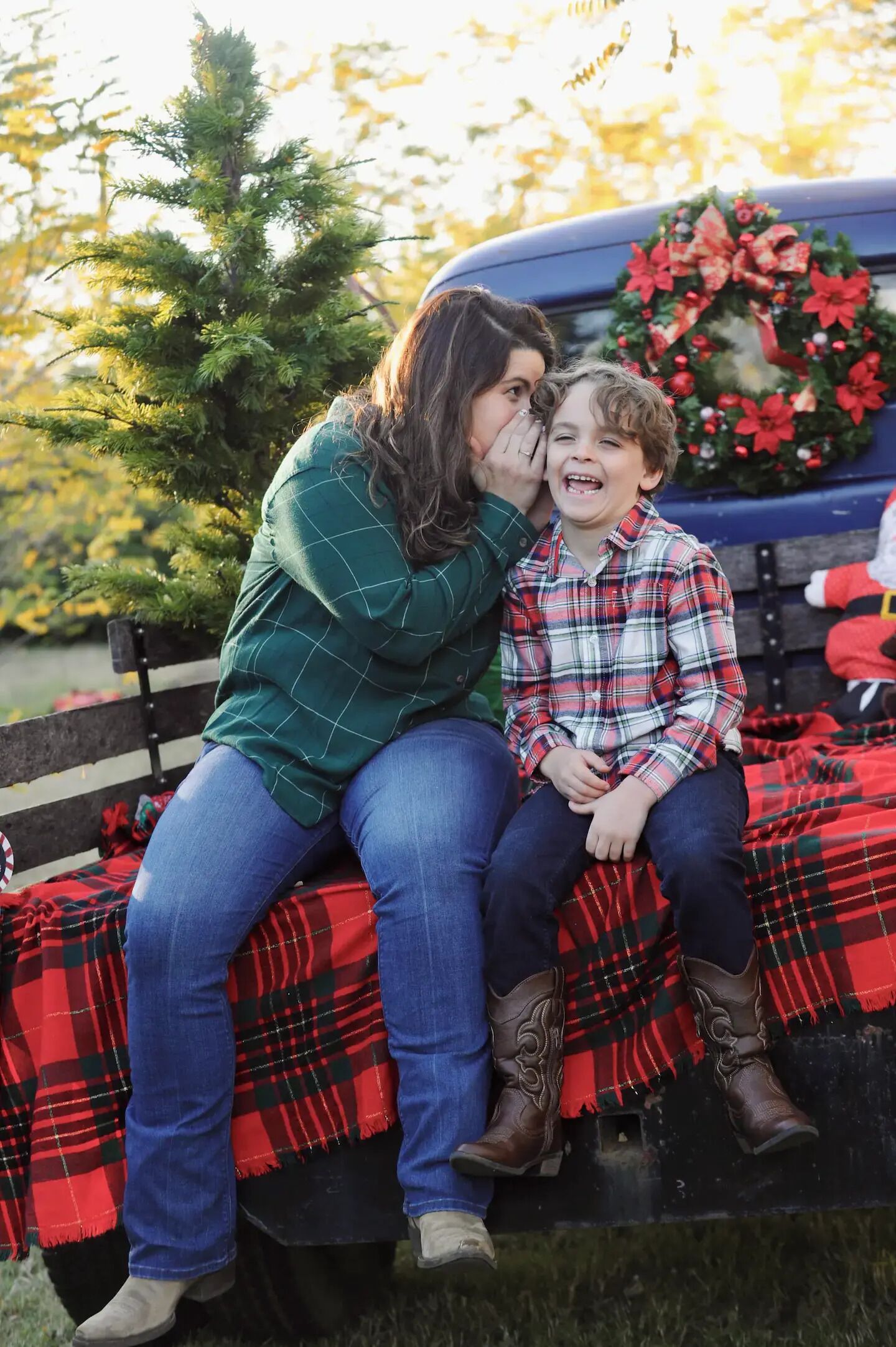 A woman and a child sitting on a bench with a Christmas wreath and poinsettia in the background.