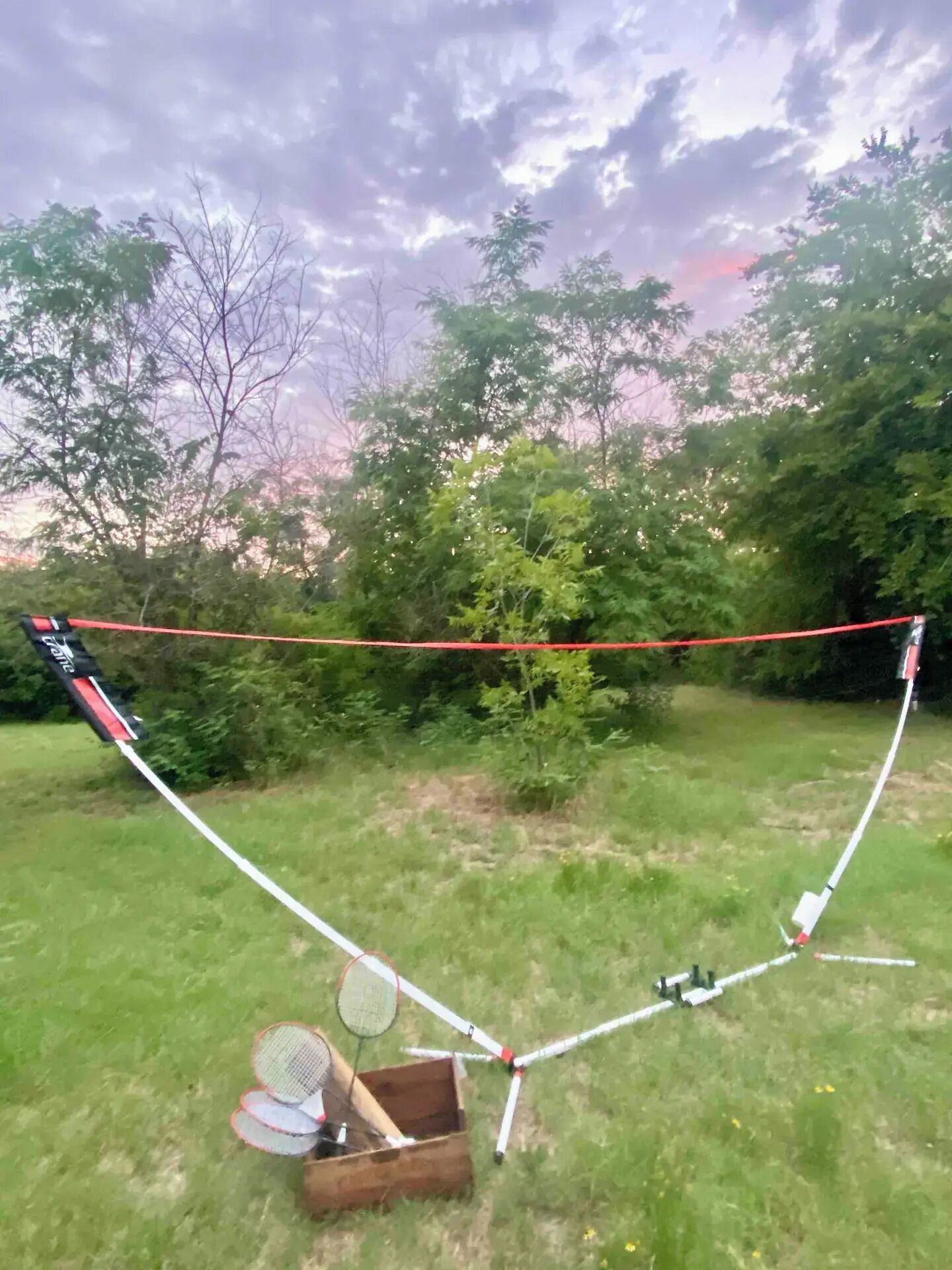 Uma pipa com estrutura vermelha e branca, montada em uma área gramada com árvores ao fundo.