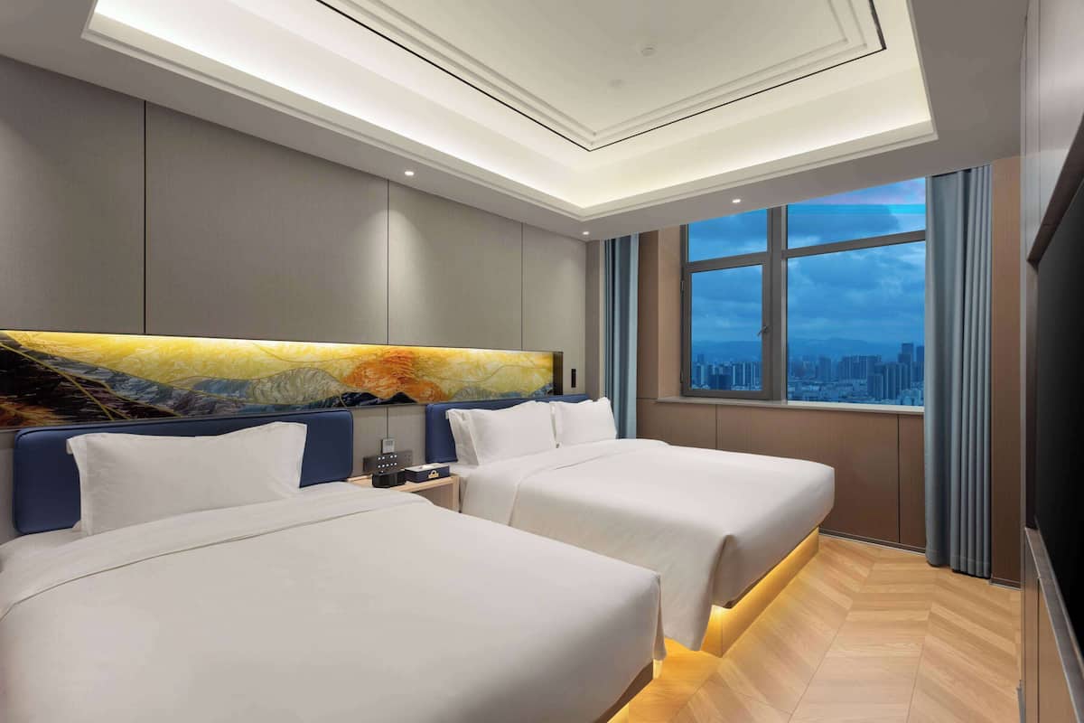 A hotel room with two beds, a city view, and a modern design.