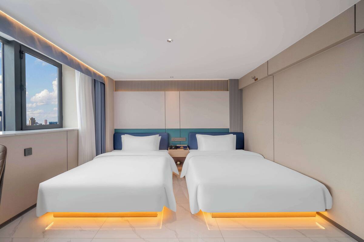 A modern hotel room with two beds, a large window, and a city view.