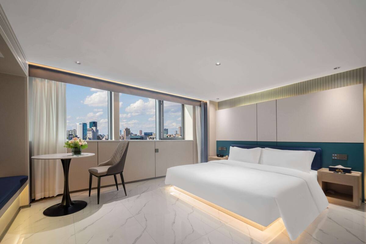 A modern hotel room with a large bed, a desk, and a view of the city skyline.