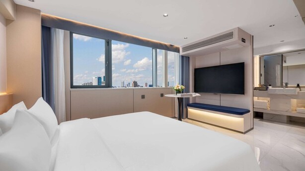 A modern hotel room with a large bed, a TV, a small table with a bench, and a city view through large windows. - Days Inn By Wyndham Kunming Wujiaba (Kunming)