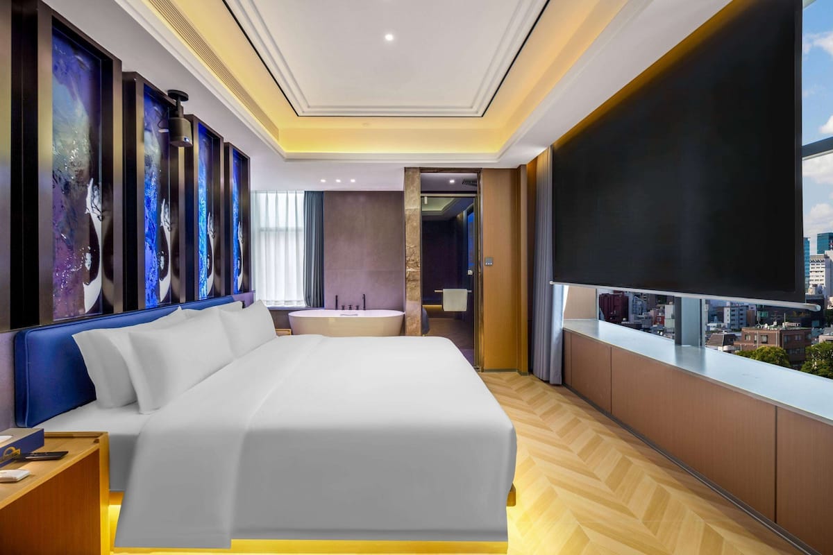A modern hotel room with a large bed, a bathtub, and a city view.