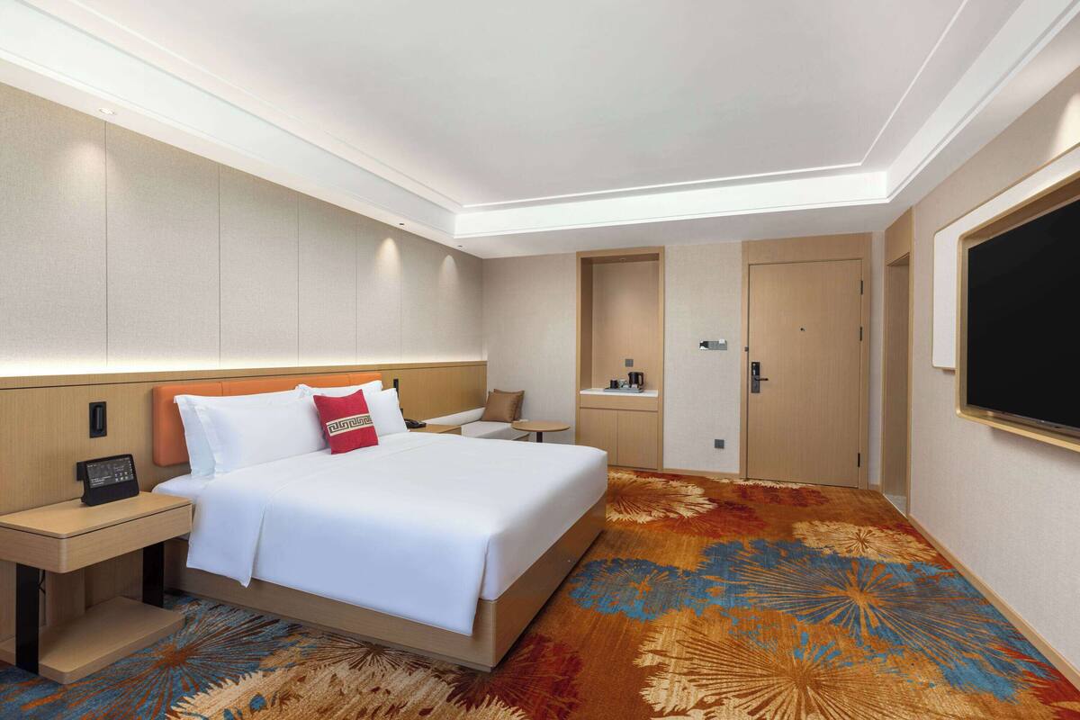 Ein Hotelzimmer mit einem großen Bett, einem Schreibtisch, einem Sessel, einem kleinen Tisch, einem Kleiderschrank und einem Fernseher.