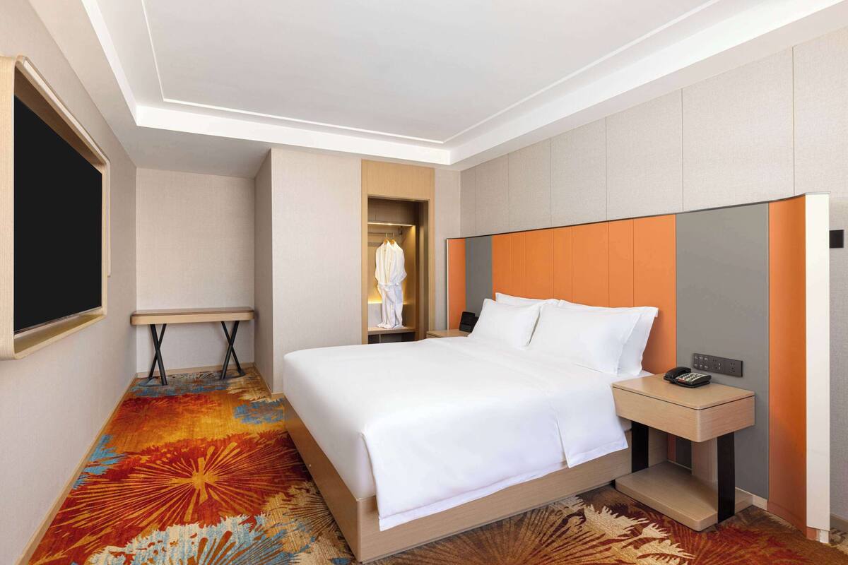 Ein Hotelzimmer mit einem großen Bett, einem Nachttisch mit Telefon und einem Kleiderschrank.