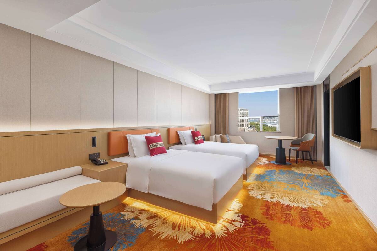Ein Hotelzimmer mit zwei Betten, einem Sofa, einem kleinen Tisch und einem Fernseher.