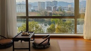 Una stanza con un'ampia finestra che si affaccia su un fiume e degli edifici. Si nota un tavolo con una sedia e un piccolo oggetto decorativo.