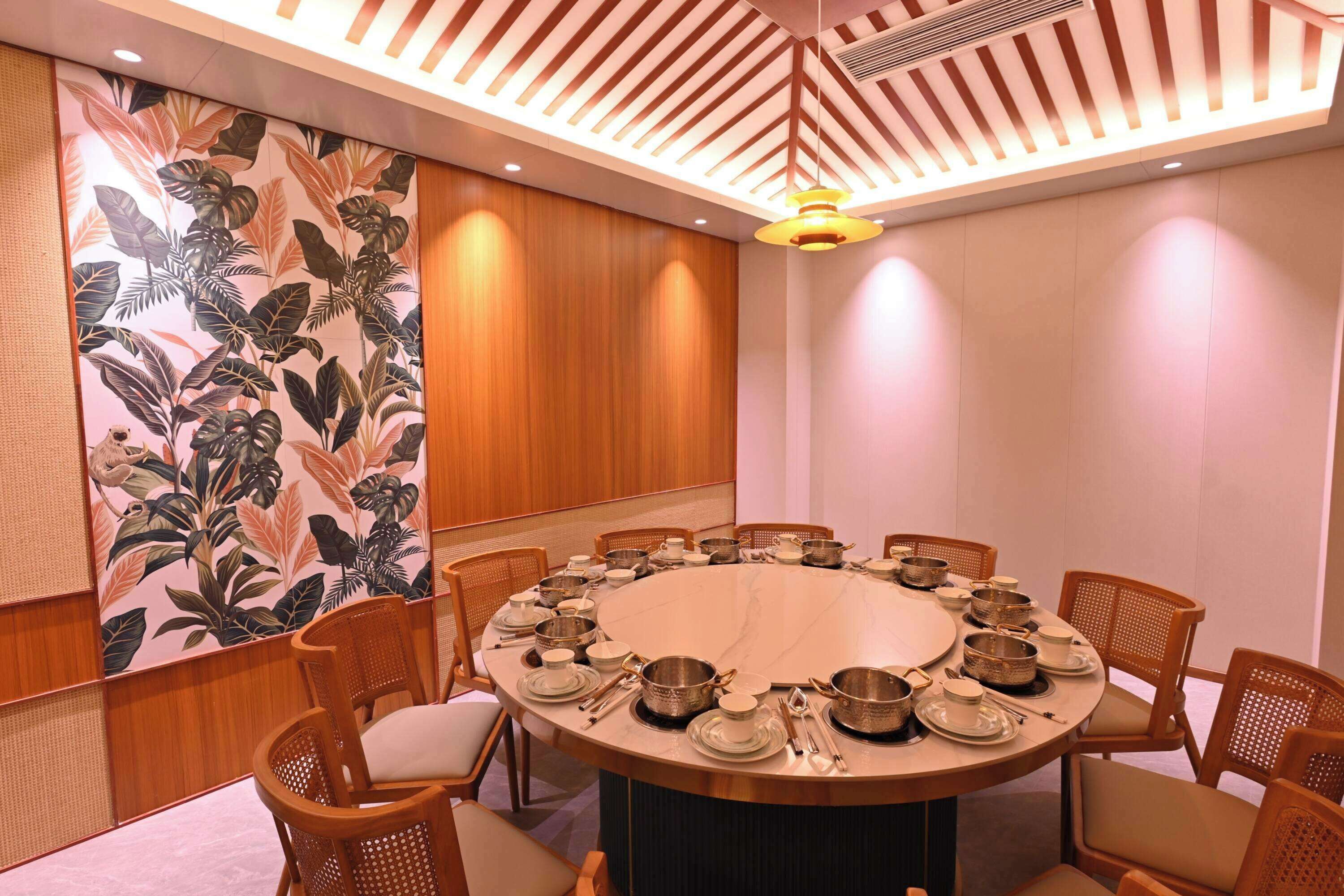 Un salón de conferencias con una mesa redonda, sillas de madera y una pared decorativa con hojas tropicales.