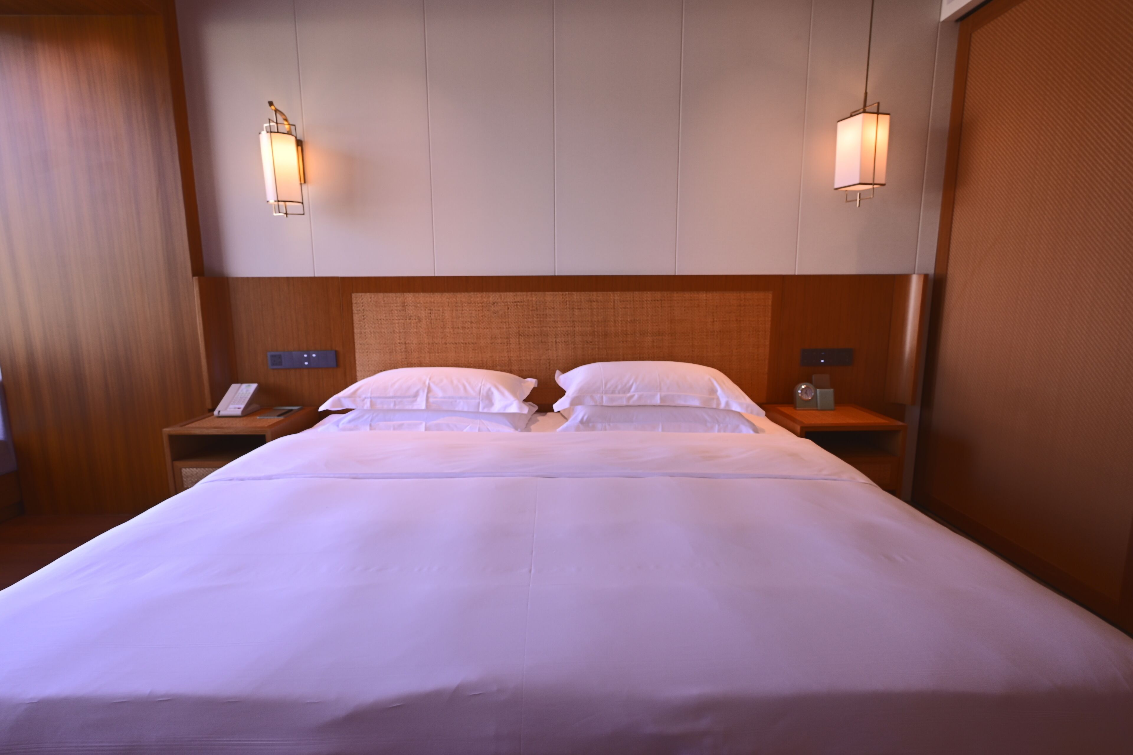 A double bed with white linens, two bedside tables, a wooden headboard, and wall-mounted lamps.