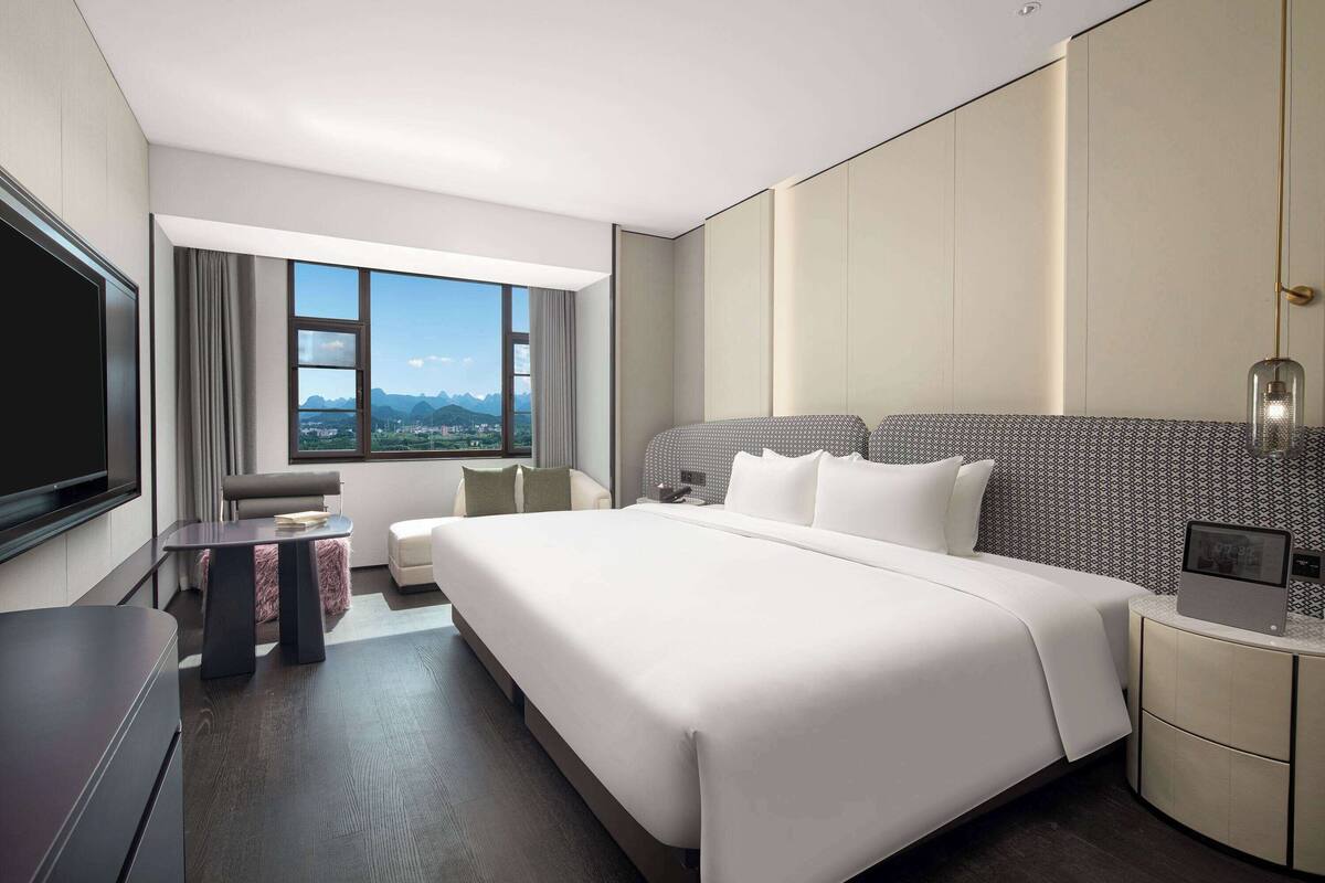 Ein modernes Hotelzimmer mit einem großen Bett, einem Schreibtisch, einem Fernseher und Blick auf die Stadt.