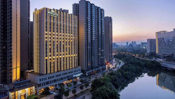 Um hotel imponente com um letreiro chamativo, vários andares e um rio em primeiro plano.