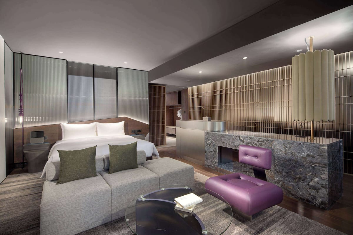Ein modernes Hotelzimmer mit einem großen Bett, einer Sitzecke mit Glastisch, einem Kamin und Blick auf die Stadt.