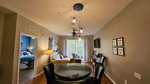 Un coin repas comprenant une table ronde et quatre chaises, un ventilateur de plafond et une fenêtre avec des rideaux.