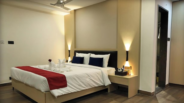 A hotel room with a bed, bedside tables, a nightstand, a red throw blanket, and a single red rose. - Sri Sri Sri Excellency  (Khammam)