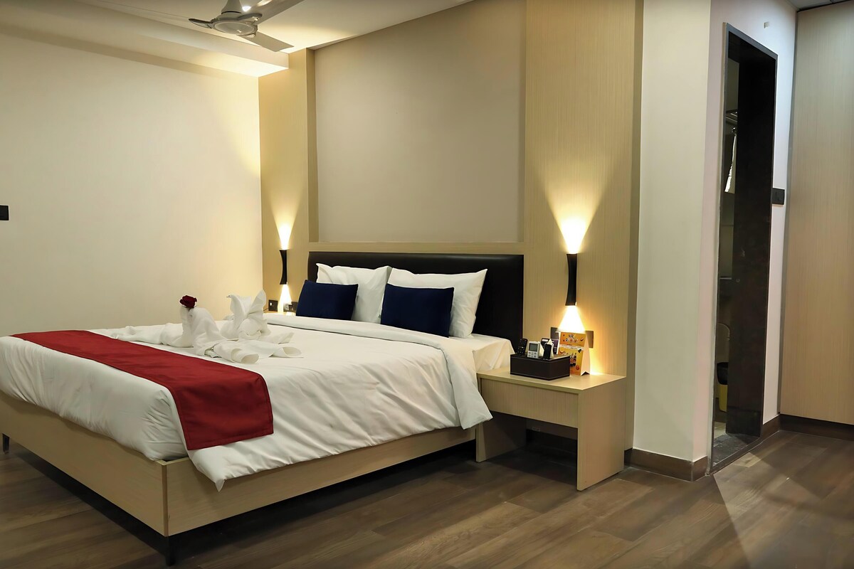 Una habitación de hotel con cama, mesitas de noche y una manta roja, además de una rosa roja.