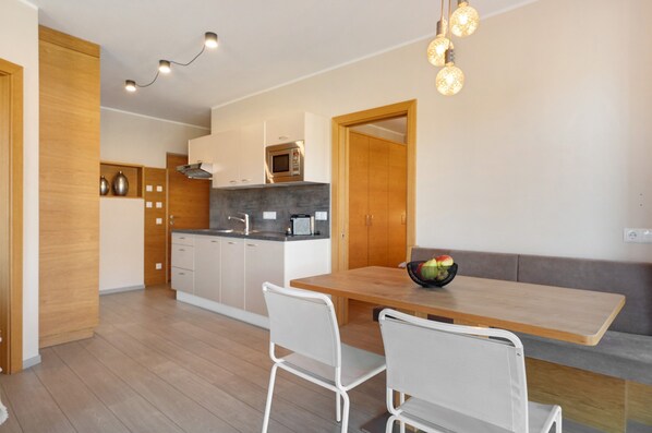 Una cucina moderna con mobili in legno, un forno a microonde e una zona pranzo con tavolo in legno e sedie bianche.