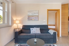 A modern living room with a grey sofa, a glass coffee table, and a painting on the wall.