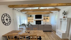 A modern kitchen with wooden beams, a dining table with chairs, a large clock, and a living area with a sofa and TV. - Relax on the Lake - 180 degree Views (North East)