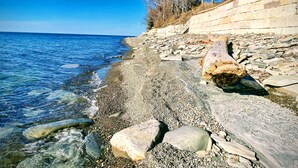 A rocky shoreline with clear blue water, a stone wall, and leafless trees. - Relax on the Lake - 180 degree Views (North East)