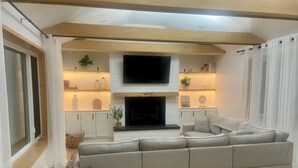 A modern living room with a large grey sectional sofa, a flat-screen TV mounted above a fireplace, and white cabinetry with shelves. - Relax on the Lake - 180 degree Views (North East)