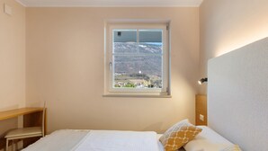 A bedroom with a bed, a desk, a chair, a window with a mountain view, and a nightlight.