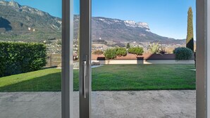 A view from a window overlooking a well-maintained lawn, a mountain range, and a distant town.