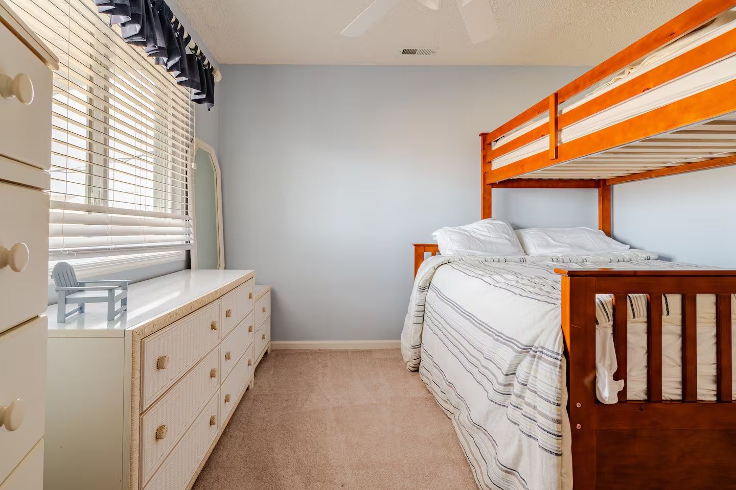 A bedroom with a bunk bed, a dresser, and a window with blinds.