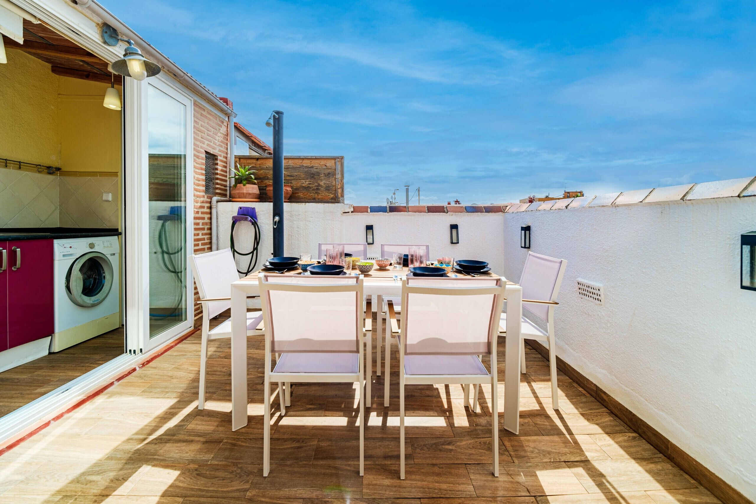 Une terrasse avec une table et des chaises, un lave-linge et un mur en briques.