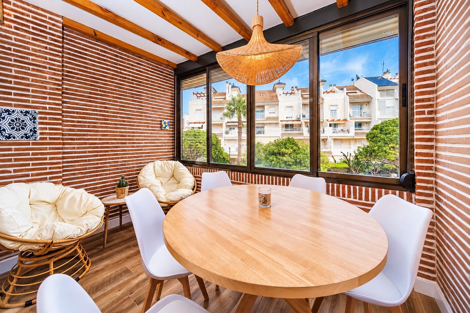 Un intérieur moderne avec une table ronde en bois, des chaises blanches, un fauteuil en osier et un luminaire suspendu.