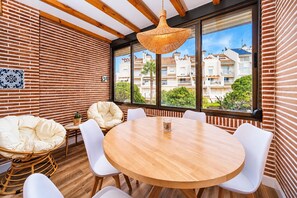 A modern interior with a round wooden table, white chairs, a wicker chair, and a hanging light fixture. - Esencia del Arenal Javea Apartment, with Sunny Terrace and next to the Beach (Javea / Xàbia)