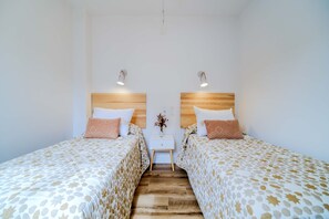 A double room with two beds, each with a wooden headboard and matching pillows. A small white nightstand with a vase of flowers is centered between the beds.