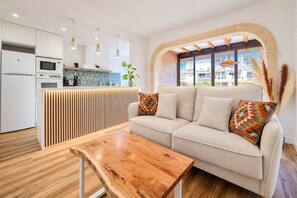 Eine moderne Küche mit integriertem Mikrowellenherd und Backofen, einem Holztisch und einer Couch mit gemusterten Kissen.