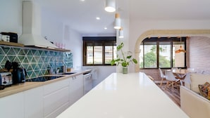 A modern kitchen with a white countertop, a built-in stove, and a backsplash with a geometric pattern. There is a dining area with a table and chairs, and a large window providing a view of the outside.