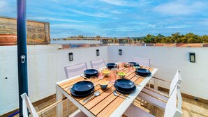 A rooftop dining area with a wooden table set for six, surrounded by white chairs.