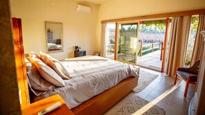 Ein Schlafzimmer mit einem großen Bett, einem Spiegel, einem Nachttisch und Blick auf eine Terrasse durch Glastüren.