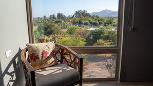 A chair with a cushion, a window with a view of a landscape, and a hanging necklace.