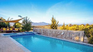 Una piscina con un muro de piedra y vistas a montañas al fondo.