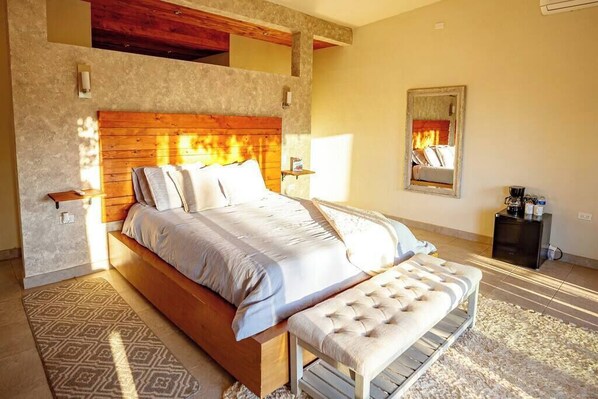 A bedroom with a large bed, a bench, a nightstand, and a wall-mounted mirror.