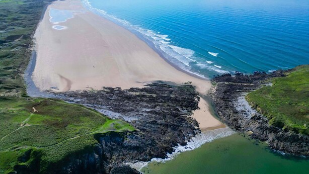 Paesaggio costiero con spiaggia sabbiosa, scogliere rocciose e vista aperta sull'oceano.