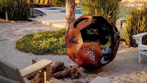A decorative soccer ball sculpture in a garden setting with a pool and lounge area in the background.