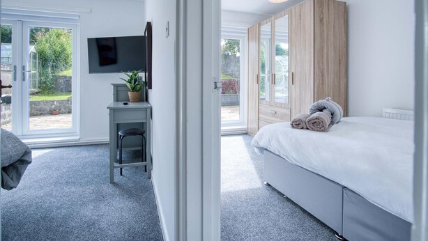 A modern bedroom with a bed, a desk with a plant, and a TV on the wall.