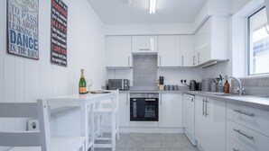 A modern kitchen with white cabinetry, a built-in oven, and a dining area with a white table and chairs.