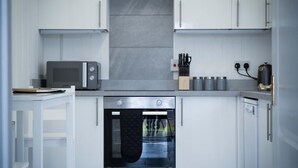 A modern kitchen with white cabinetry, a built-in oven, a microwave, and a coffee maker.