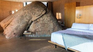A bedroom with a large rock formation, wooden walls, a bed, and a small table.