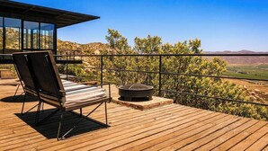 A wooden deck with a lounge chair and a fire pit, overlooking a scenic landscape.