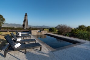 Relax by the serene pool, surrounded by lush hills and a clear sky.