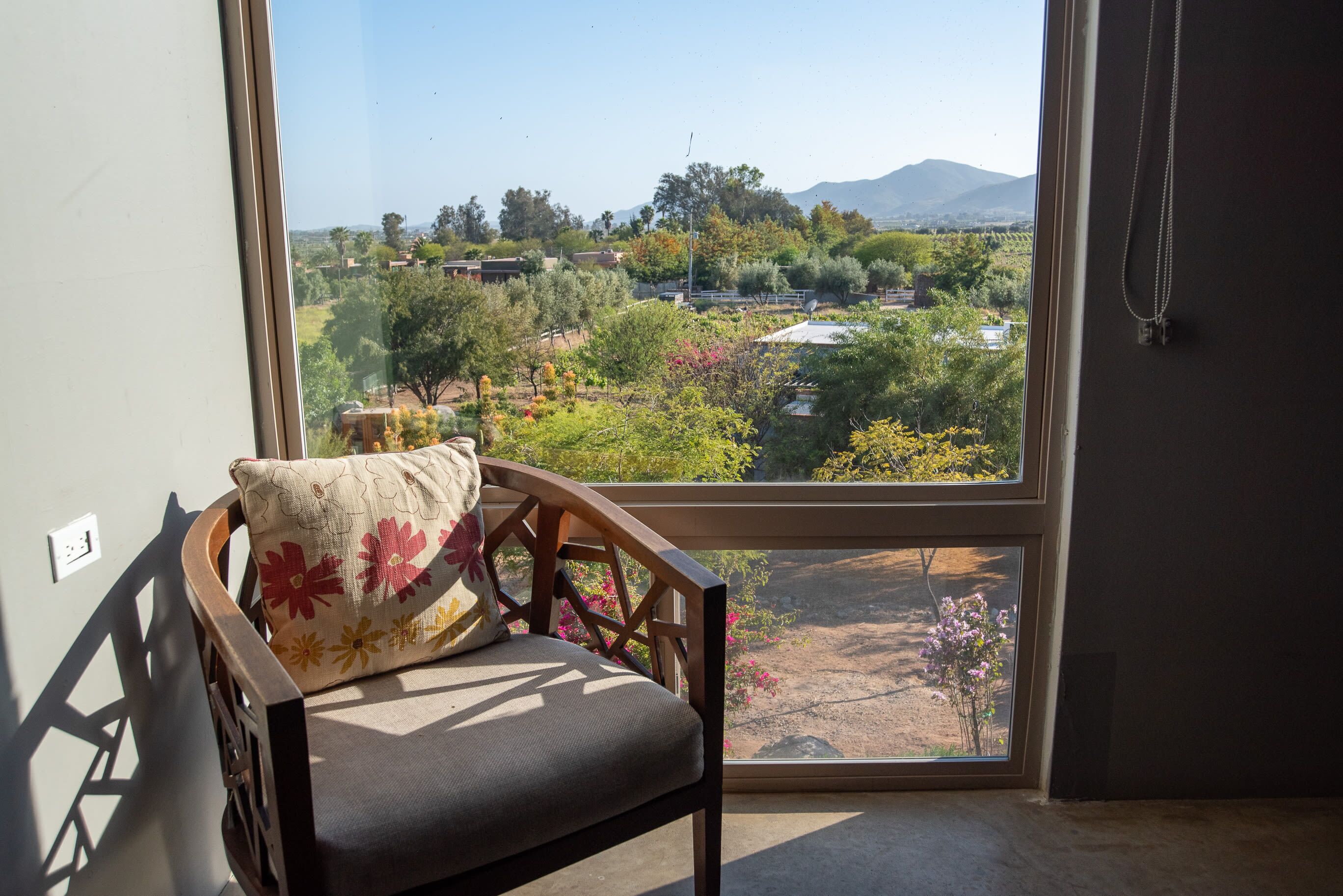 A chair with a cushion, a window with a view of a landscape, and a hanging necklace.
