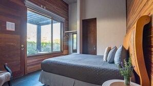 Een slaapkamer met een groot bed, een houten deur en een raam met uitzicht op groen.