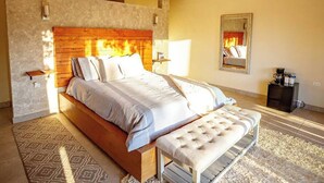 A bedroom with a wooden headboard, a large bed, a bench, and a fireplace in the background. - Vinyard Cabin - Luna del Valle (Valle de Guadalupe)