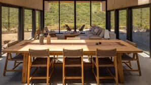 Een ruime eethoek met een lange houten tafel en geweven stoelen, met uitzicht op een prachtig landschap.